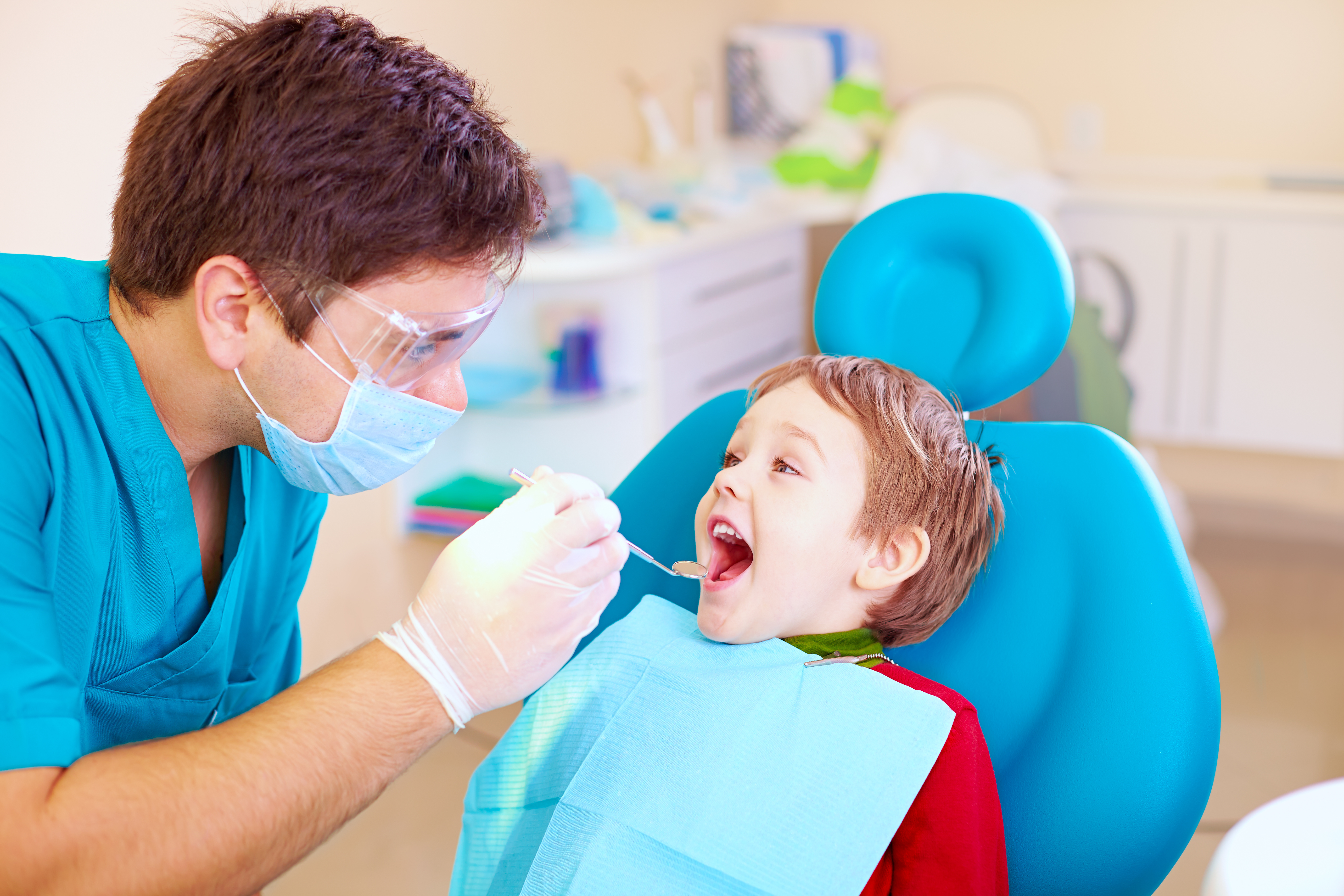 child in dentist chair with dentist looking at his teeth